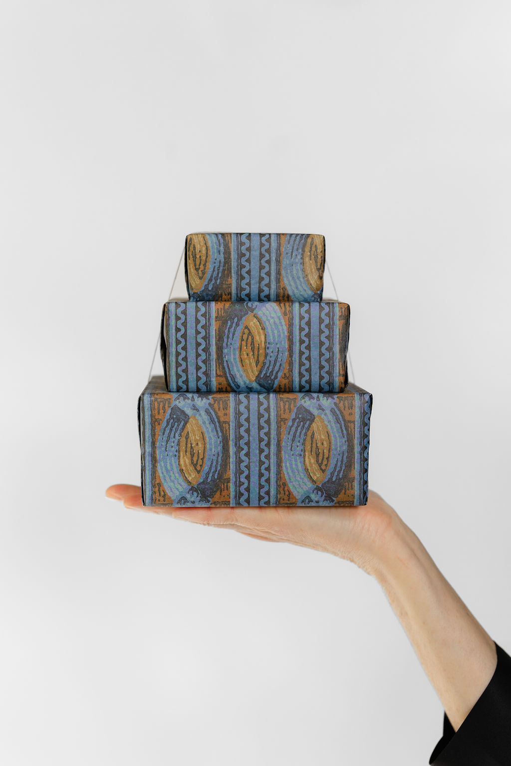 Stack of three blue wallpaper patterned boxes held by a hand against a white background