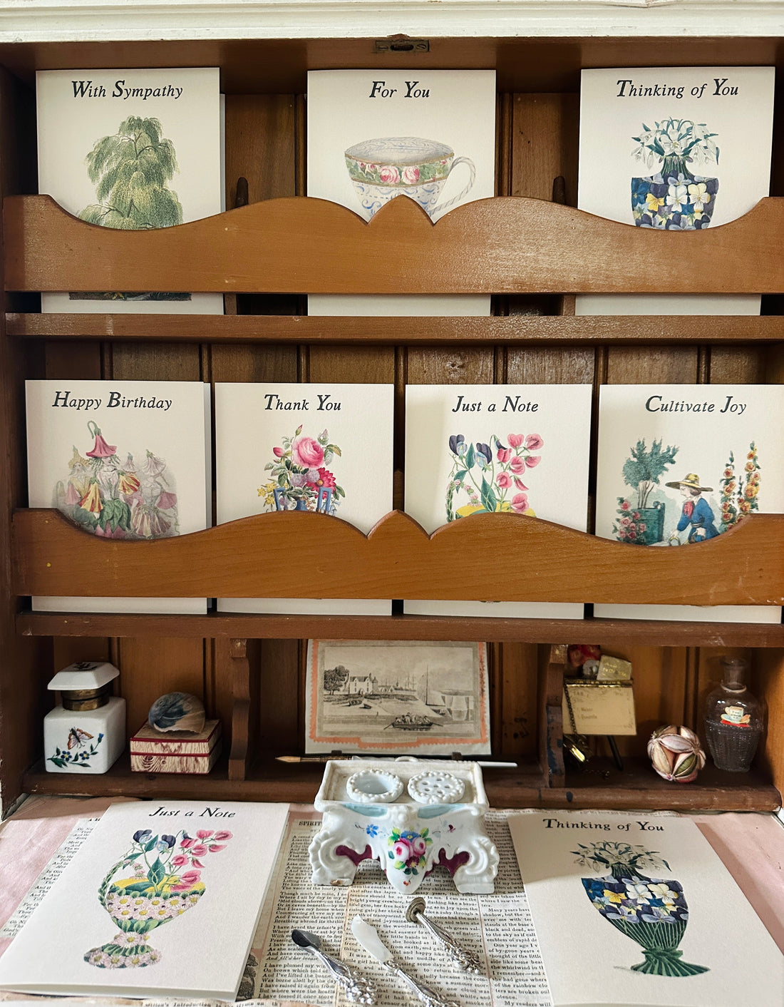 Vintage-inspired greeting cards arranged on an antique writing desk, surrounded by inkwells, a quill, and other period writing accessories.