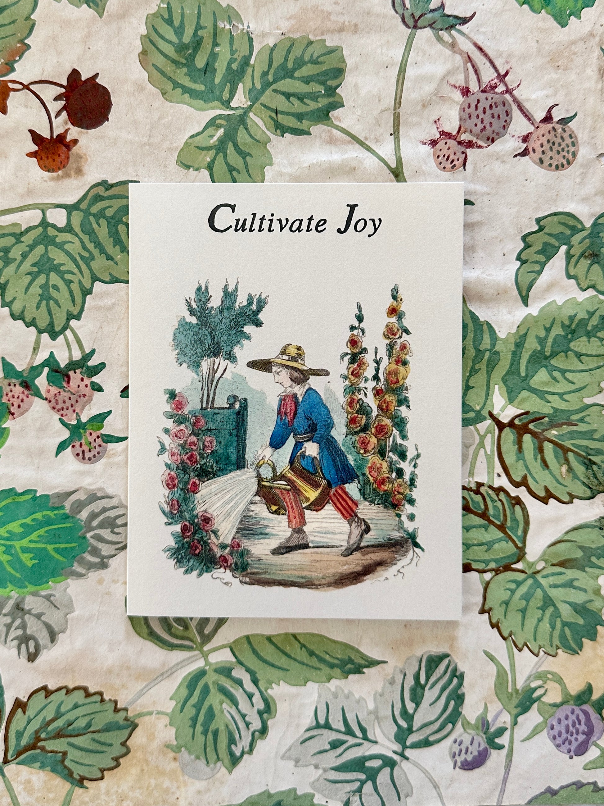 Cultivate Joy card with garden scene illustration displayed against antique French strawberry vine wallpaper, by Caldwell's Miscellaneous Fancy Goods.